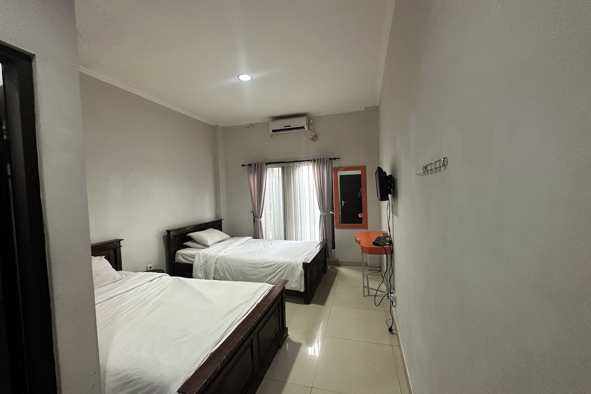 A hotel room with two beds, a small table, a chair, an air conditioning unit, and a TV.