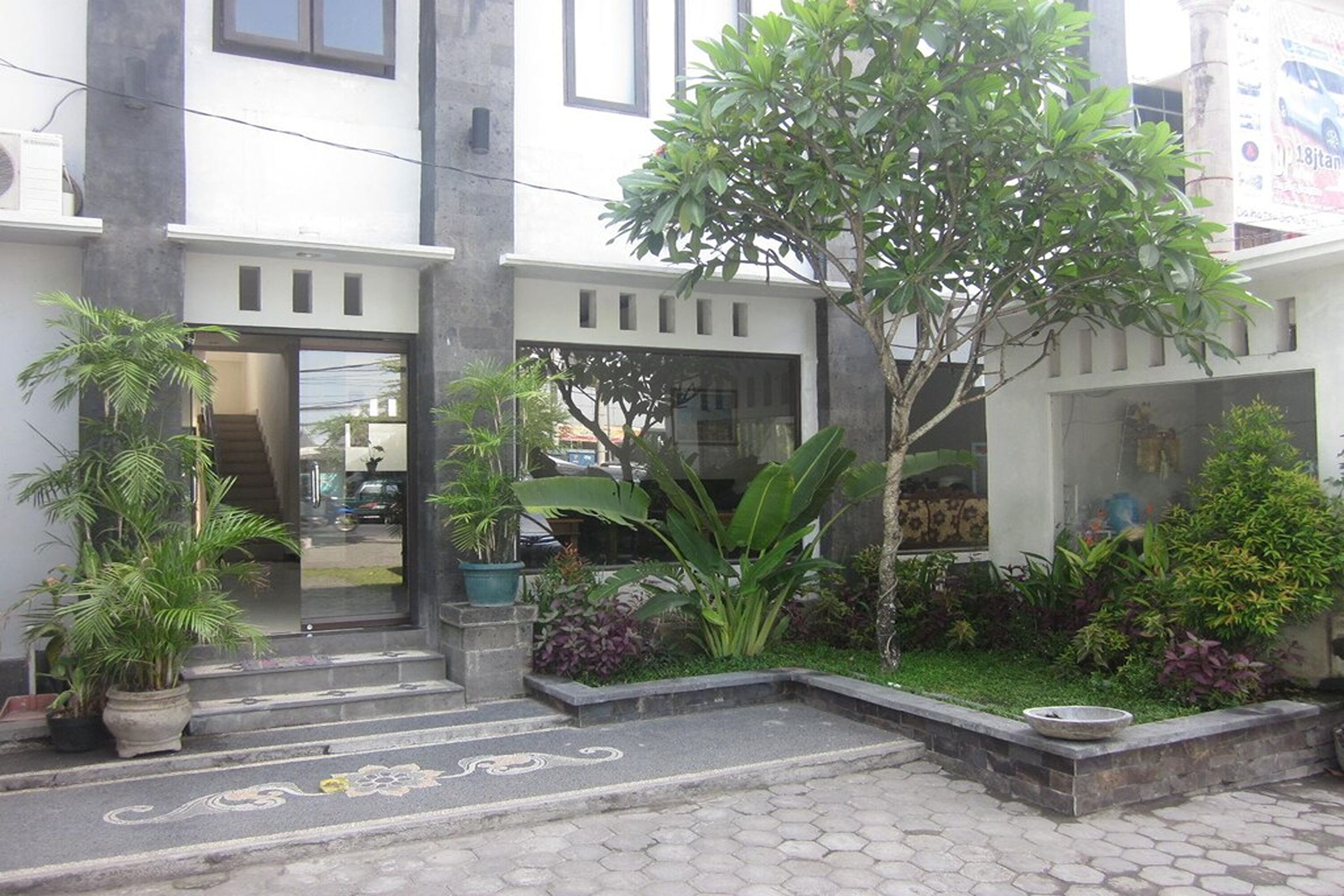 A modern building with a staircase leading to a glass door, surrounded by potted plants and a small garden area.