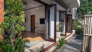 Una casa moderna con piso de madera, puerta de cristal y un pequeño jardín con plantas y fuente de agua.