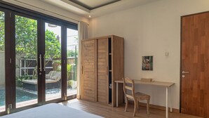 Un dormitorio con una cama grande, armario de madera, escritorio y silla, y un puerta corrediza de vidrio que da a una zona de piscina.
