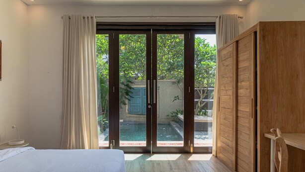Un dormitorio con cama, armario de madera y puerta corrediza de vidrio que da a una zona de piscina.