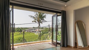 Una habitación con un gran ventanal corredero que da a un balcón con vistas a un paisaje verde y una palmera.