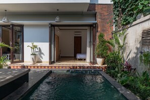 A modern outdoor pool area with a clear view into the house, a small garden, and a patio with a table and chairs. - Villa Prasuci (Canggu)