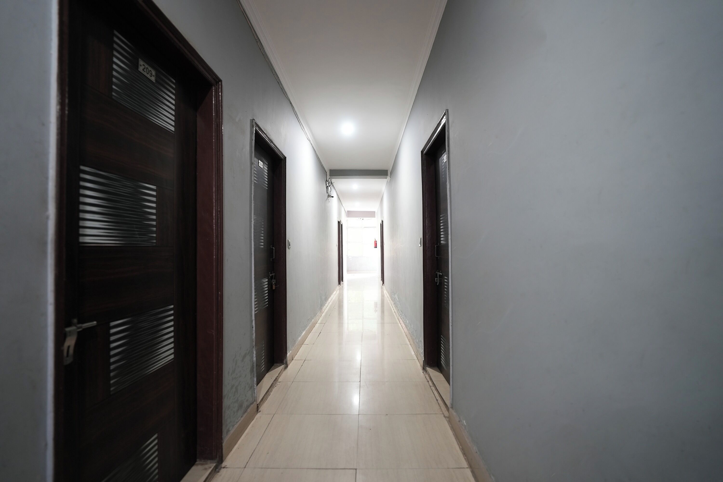 Un long couloir étroit, avec des portes de chaque côté, qui mène à une pièce lumineuse au bout.