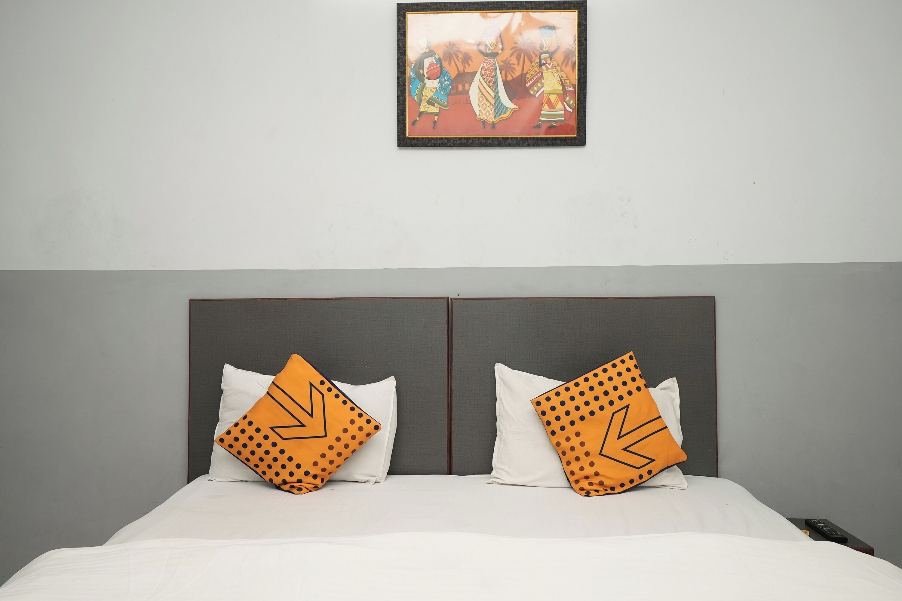 Habitación de hotel con una cama, dos almohadas de estampado geométrico, un cuadro en la pared y una pared gris lisa.