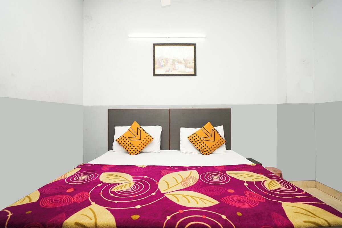 Habitación de hotel con cama, dos almohadas, un cuadro en la pared y una colcha estampada.