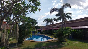 A swimming pool surrounded by palm trees and cacti, with a building in the background. - Kanchira Resort (Pattaya)