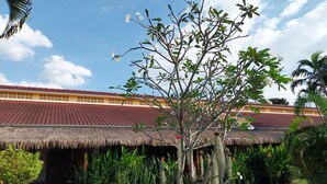 A traditional thatched-roof building with a red-tiled roof, surrounded by lush greenery and cacti. - Kanchira Resort (Pattaya)