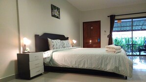 A bedroom with a bed, bedside tables, a nightstand, a door, and a view of greenery outside. - Kanchira Resort (Pattaya)