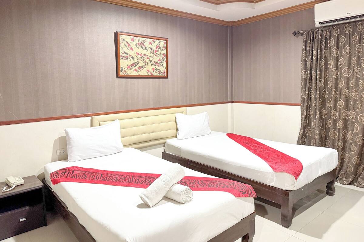 A hotel room with two beds, a telephone on the nightstand, and a wall-mounted air conditioner.