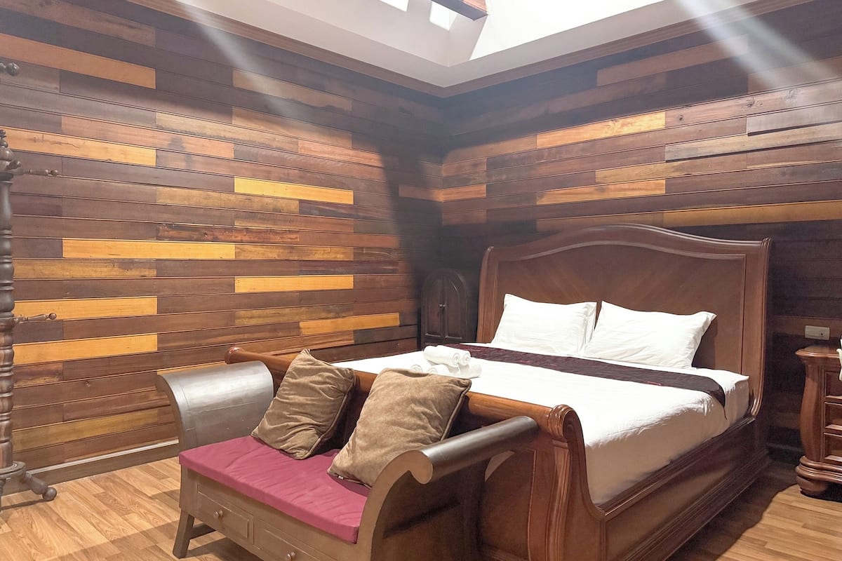 A bedroom with a wooden bed, a bench with cushions, and a sloped ceiling with skylights.