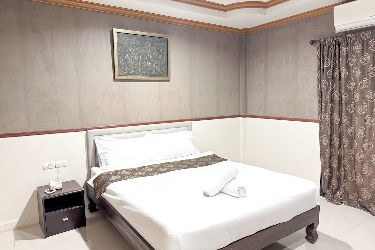 A neatly made bed with white linens, a small bedside table with a phone, and a patterned curtain.