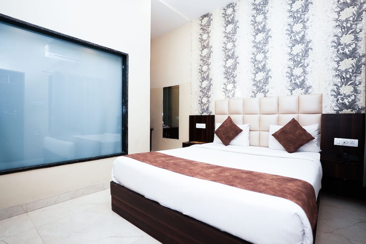 Quarto de hotel moderno com uma cama grande, uma mesa de cabeceira, um espelho e uma janela com vista para o exterior.