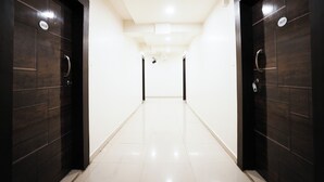 A hallway with dark wooden doors, white walls, and a tiled floor. - The White House (Pune)