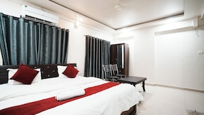 A hotel room with a large bed, a desk, a chair, an air conditioning unit, and a mirror. - The White House (Pune)