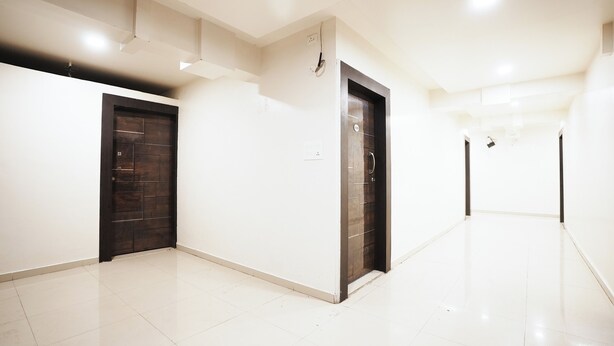 A hallway with two doors, one dark and one light, leading to rooms. The floor is tiled, and the walls are plain. - The White House (Pune)