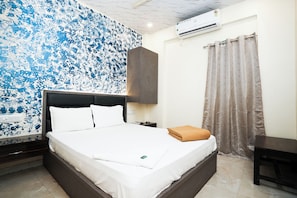 A neatly made bed with white linens, a brown headboard, and a folded brown towel on the side. - The United Hotel (Mumbai)