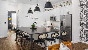 A modern kitchen with a central island, black pendant lights, white cabinets, and stainless steel appliances.