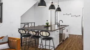 A modern kitchen with a central island, black pendant lights, and a white backsplash.