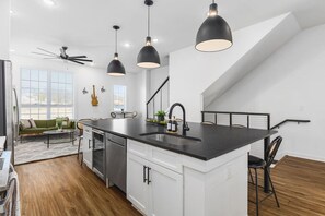 A modern kitchen with a central island, pendant lighting, and a staircase leading to an upper level. - Modern Home with Large Patio, Rooftop Deck & Garage (Nashville)