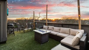 A rooftop patio with a sofa, chairs, and a grill.