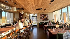 A restaurant with wooden ceiling, bar area, and seating for guests.
