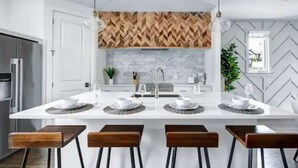 Una cocina moderna con una isla central, armarios blancos y un salpicadero con motivo de espiga.