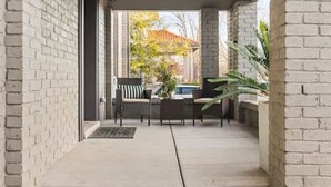 A covered outdoor area with a brick wall, a seating arrangement, and a view of a residential area.
