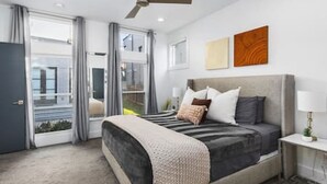 Une chambre moderne avec un grand lit, un ventilateur de plafond et une vue sur l’extérieur, visible à travers la porte vitrée.