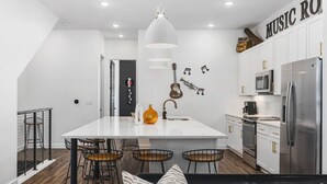 A modern kitchen with white cabinets, stainless steel appliances, and a central island with bar stools. - Rooftop Deck, Patio & Garage - Walk to Restaurants (Nashville)