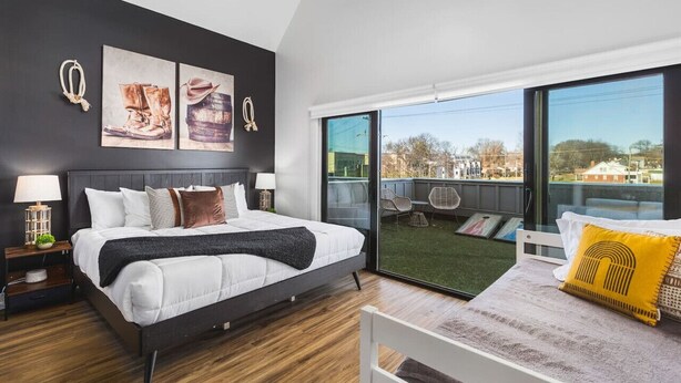 A modern bedroom with a large bed, a balcony with a view, and artwork on the wall. - Rooftop Deck, Patio & Garage - Walk to Restaurants (Nashville)