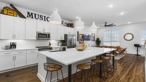 A modern kitchen with white cabinetry, a central island with bar stools, pendant lighting, and a ceiling fan. - Rooftop Deck, Patio & Garage - Walk to Restaurants (Nashville)
