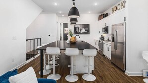 Una cocina moderna con una isla central, taburetes blancos de bar y una lámpara colgante.