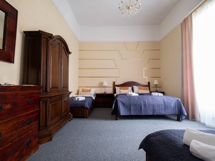 A hotel room with a large wooden dresser, two beds with blue bedding, a chandelier, and a patterned wall.