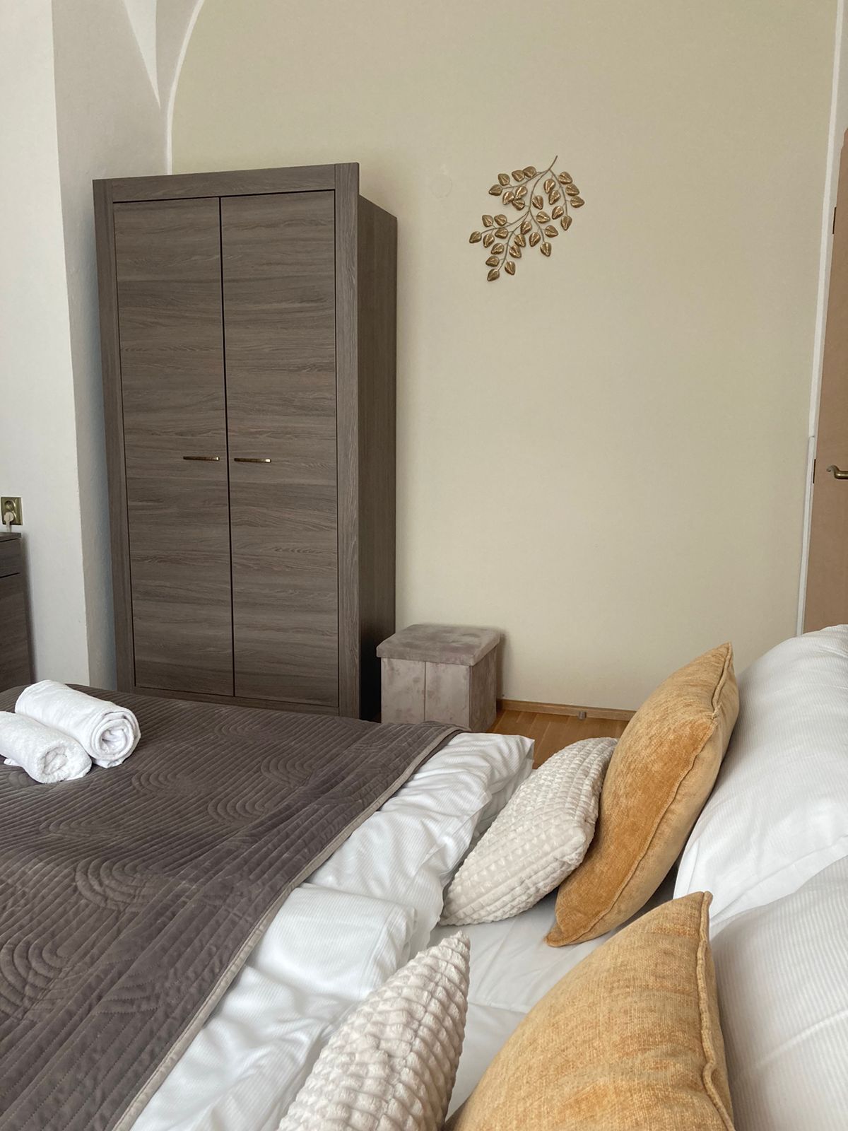 A modern bedroom with a large wardrobe, a small stool, and neatly arranged pillows.
