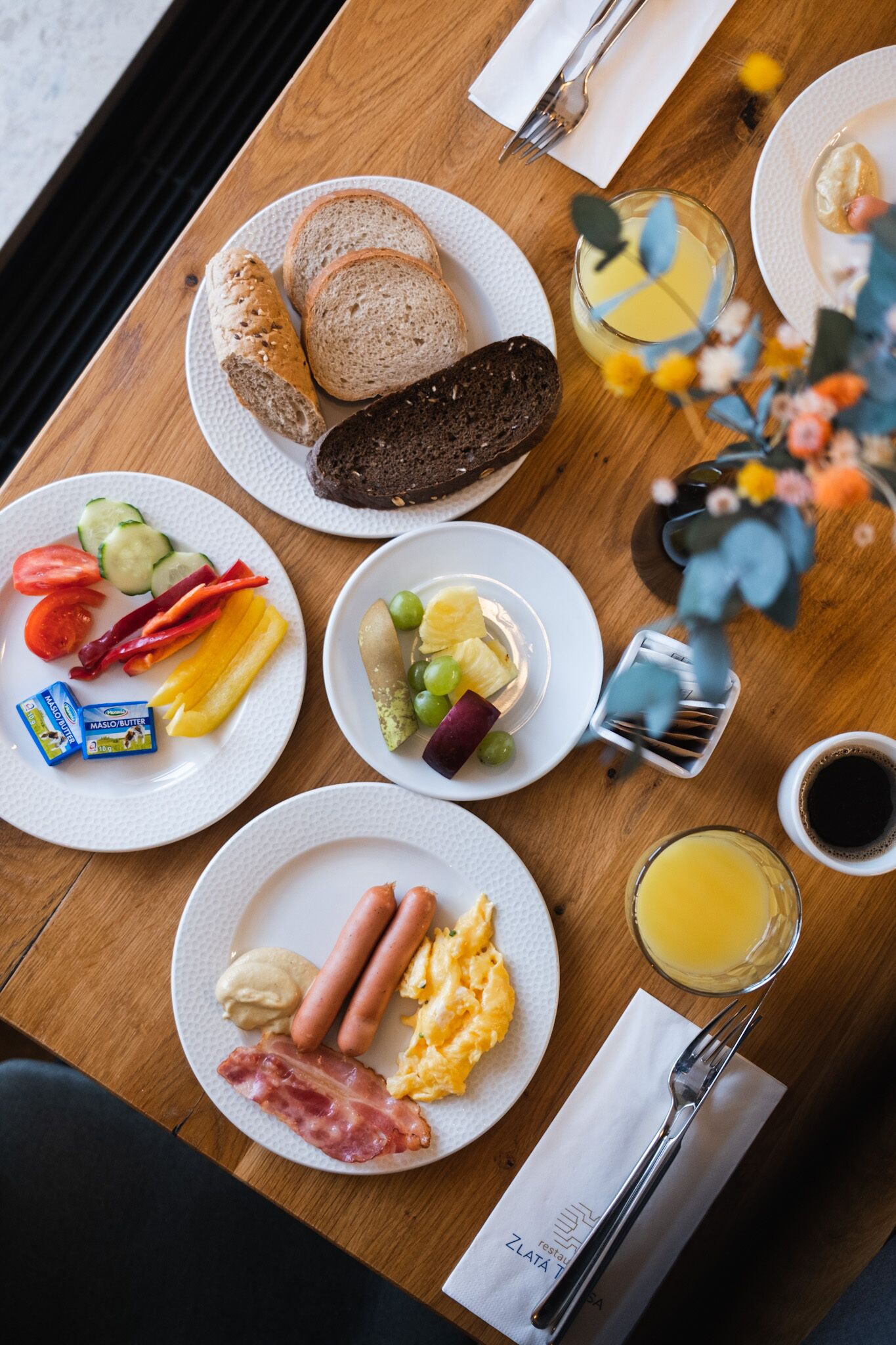 A breakfast table with various food items, including bread, eggs, sausages, and vegetables.