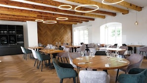 Un comedor moderno con mesas y sillas de madera, un revestimiento de pared con patrón de espiga e iluminación colgante.