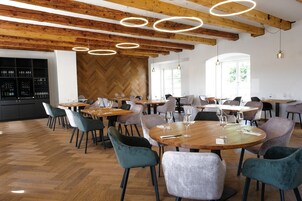 A modern dining area with wooden tables and chairs, a herringbone-patterned wall, and pendant lighting.