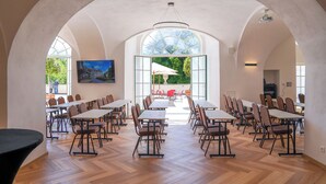 Un comedor amplio con techos altos y ventanas grandes, con varias mesas y sillas dispuestas para comer.