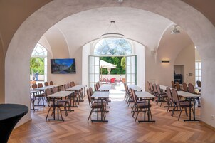 A spacious dining area with high ceilings and large windows, featuring multiple tables and chairs arranged for dining.