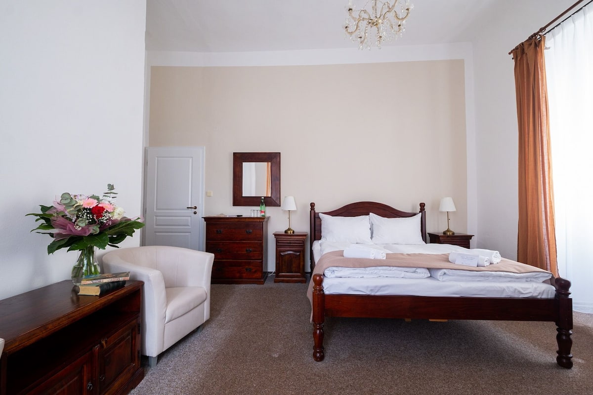 A hotel room with a wooden bed, a chair, a dresser, a mirror, and a vase of flowers.