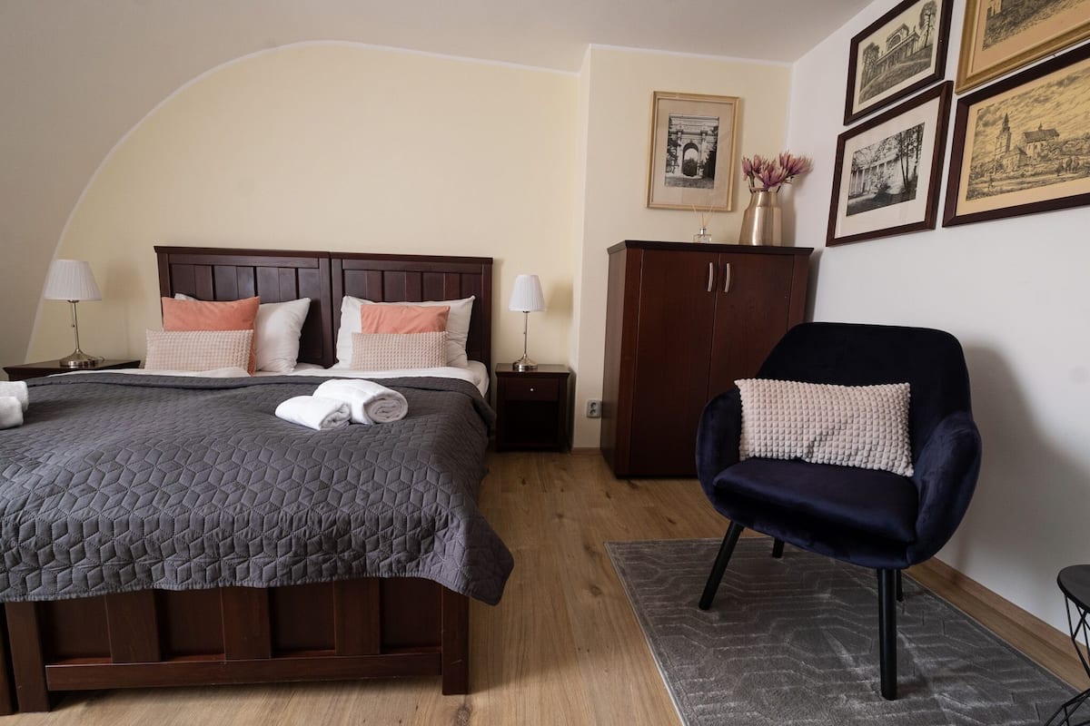 A bedroom with a bed, a chair, a wardrobe, and framed pictures on the wall.