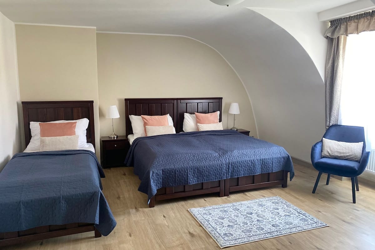 A hotel room with two beds, a blue chair, a patterned rug, and a curved ceiling.