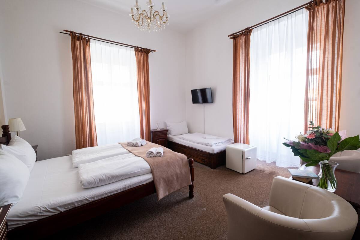 A hotel room with a bed, a bedside table, a TV, a chair, and a desk with a vase of flowers.
