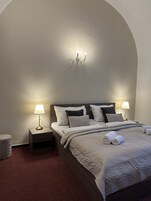 A neatly made bed with a grey quilt, two bedside lamps, and a small bedside table.