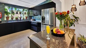 Une cuisine moderne dotée d’un îlot central, d’appareils électroménagers en acier inoxydable et offrant une vue sur l’extérieur.