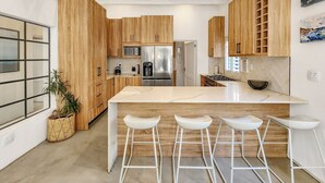Eine moderne Küche mit Holzschränken, einer zentralen Kochinsel mit Barhocker und einem Edelstahlkühlschrank.