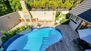 A swimming pool with a stone and tile border, surrounded by a patio with outdoor furniture. - Clivia - Pinoak Self-catering Cottages (Cape Town)