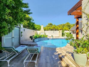 Un patio trasero con piscina, sillas de descanso y un muro de piedra.