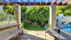 A covered patio area with a bench, a table, and a pool. - Clivia - Pinoak Self-catering Cottages (Cape Town)
